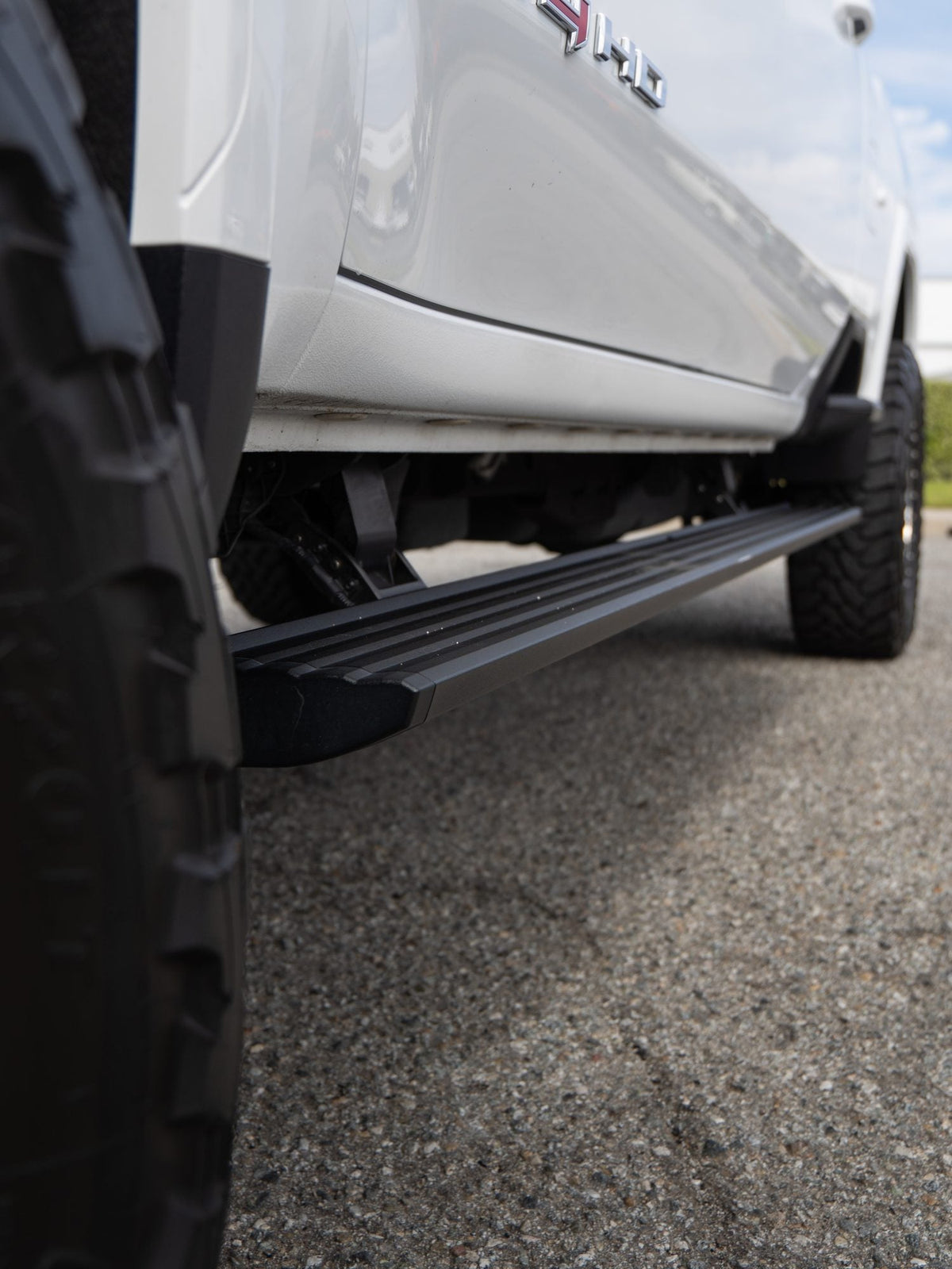 AMP Research PowerStep running board deployed on a white GMC Sierra 2500 HD AT4 upgraded by Empire Motorsports & LINE-X in Rancho Cucamonga