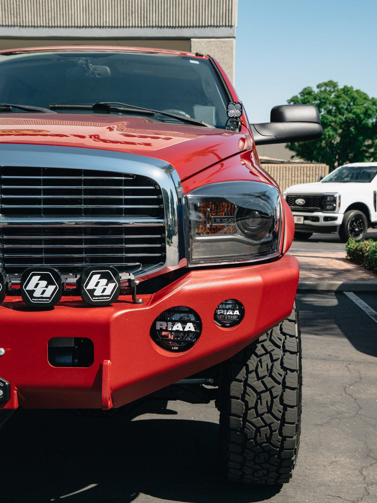 Front end of a red Dodge Ram HD with a TrailReady bumper and Baja Designs and PIAA lights, built by Empire Motorsports & LINE-X in Rancho Cucamonga