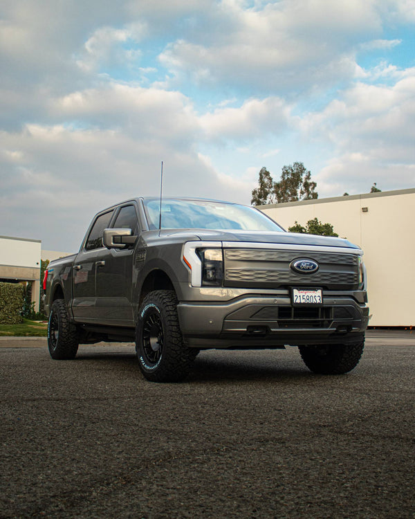 Front three-quarter view of a gray Ford F-150 Lightning parked under a cloudy sky
