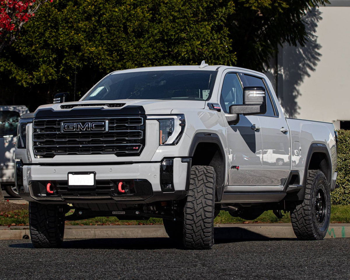 Front view of a silver GMC Sierra HD AT4 with a black grille and red tow hooks