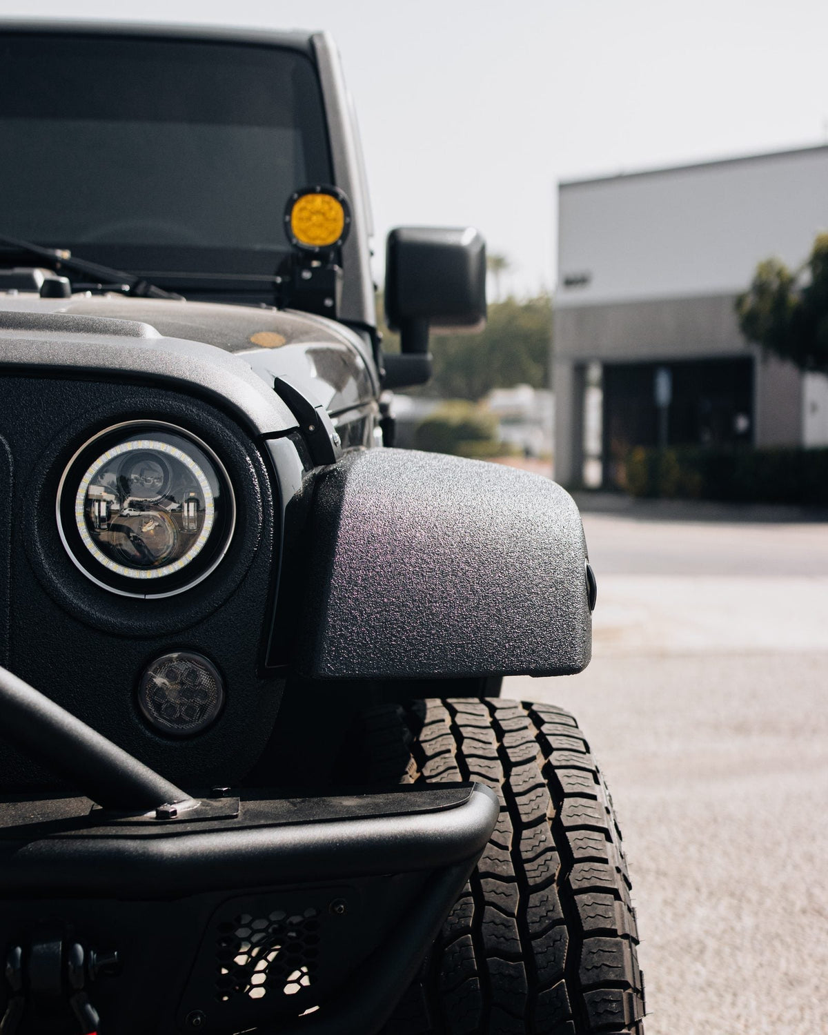 Close-up of the headlight, fender and all-terrain tire on a black Jeep Wrangler Rubicon built by Empire Motorsports & LINE-X in Rancho Cucamonga