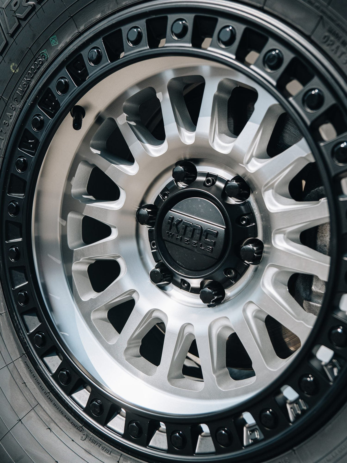 Close-up of a silver KMC wheel with a black bead ring on a white truck with a BDS Suspension lift, built by Empire Motorsports & LINE-X in Rancho Cucamonga