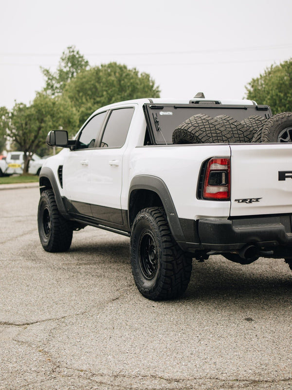 Rear three-quarter view of a white Ram 1500 TRX with black wheels and a BAKFlip folding bed cover, built by Empire Motorsports & LINE-X in Rancho Cucamonga