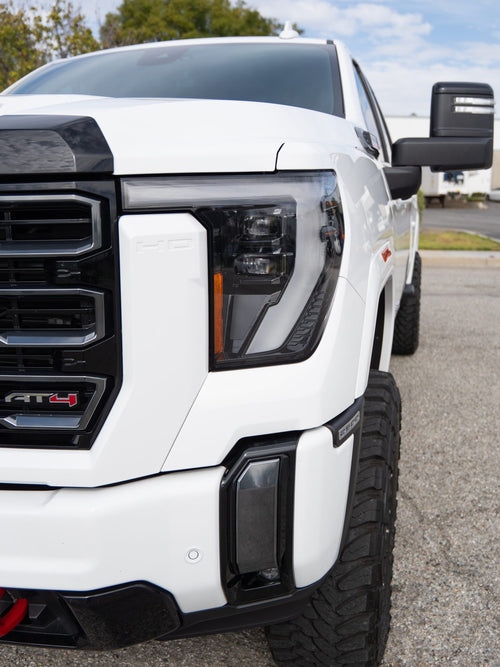 Close-up of the LED headlight and AT4 badge on a white GMC Sierra 2500 HD