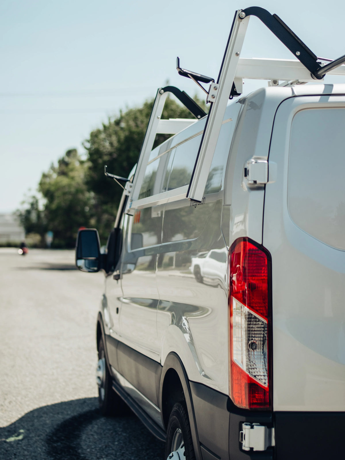 White commercial van equipped with an Adrian Steel ProLift ladder rack for easier loading and unloading.