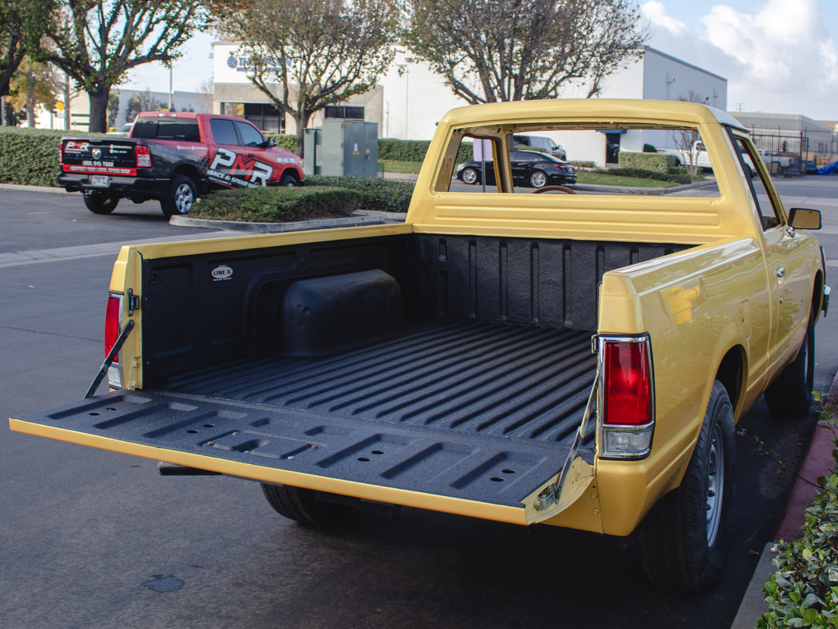 A yellow pickup truck with its tailgate open, showing a black textured bed liner installed in an outdoor parking lot setting.