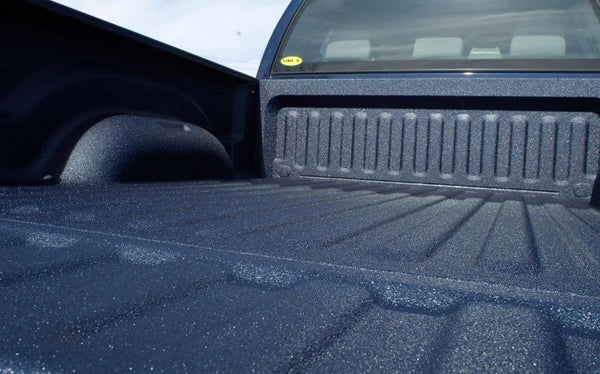 Close-up of a dark blue textured truck bed liner installed inside a pickup truck bed, showing the liner's ribbed pattern and protective coating.