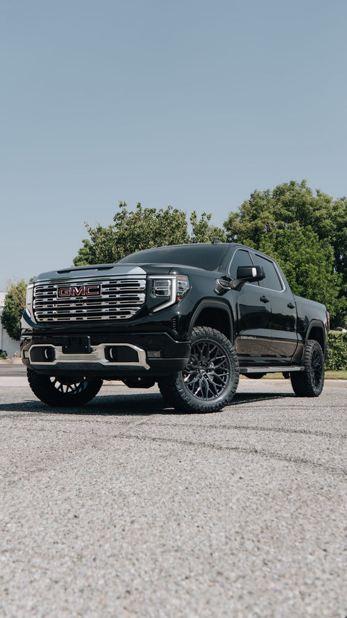 Front three-quarter view of a black GMC Sierra Denali with a BDS lift and Vossen wheels on a sunny lot