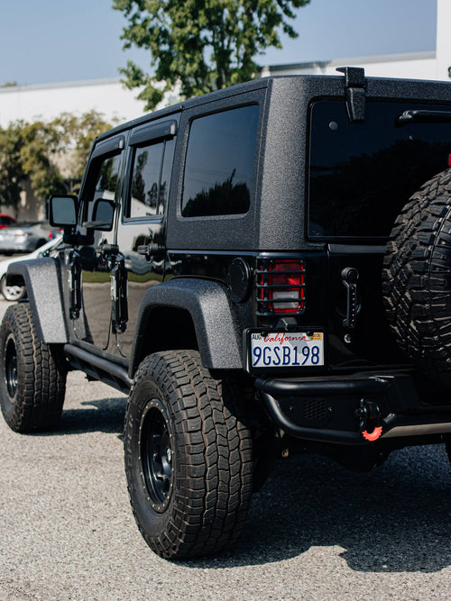 Rear three-quarter view of a black Jeep Wrangler showing the rear-mounted spare tire and tail light