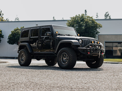Front three-quarter view of a black Jeep Wrangler Rubicon with a winch bumper parked outside a building