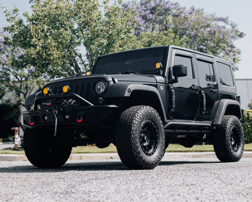Front three-quarter view of a black Jeep Wrangler Rubicon with amber bumper lights and all-terrain tires