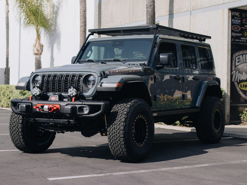 Front three-quarter view of a black Jeep Wrangler Rubicon with a roof rack, winch bumper and Baja Designs lights