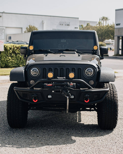 Front view of a black Jeep Wrangler Rubicon with a Warn winch bumper and amber lights