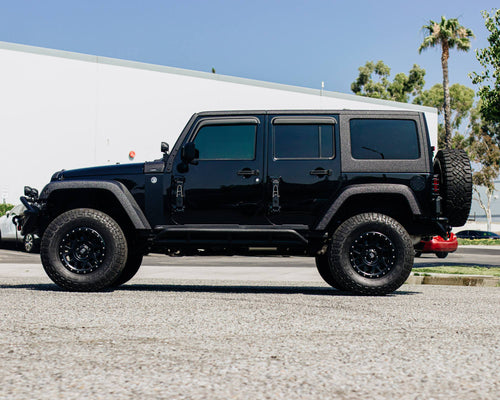 Side profile of a black Jeep Wrangler Unlimited with black wheels and a rear-mounted spare tire