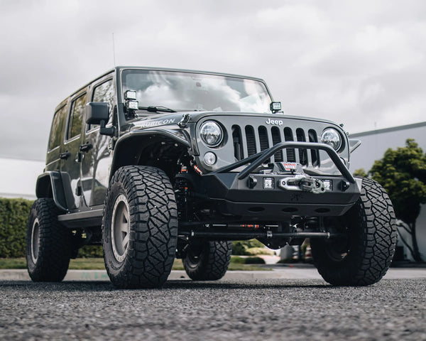 Black Jeep Wrangler with a steel off-road bumper, WARN winch, auxiliary lights, and upgraded suspension