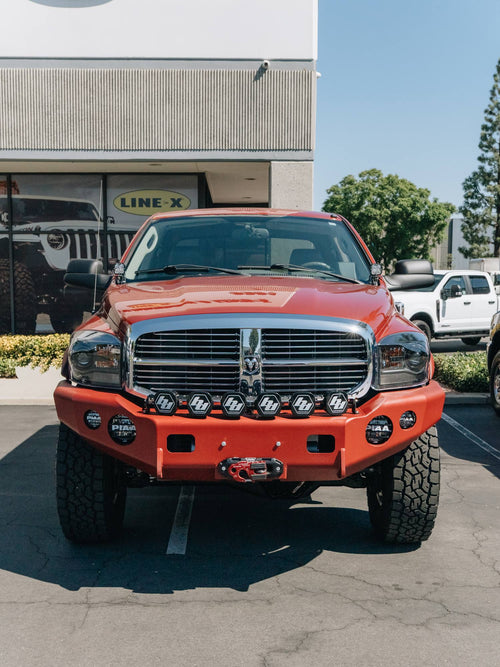 Front view of a red Dodge Ram HD with a bumper-mounted winch and Baja Designs and PIAA lighting