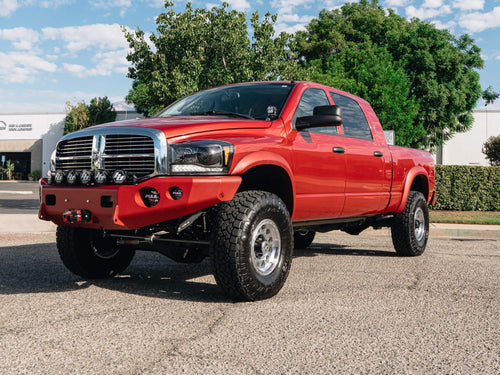 Front three-quarter view of a red Dodge Ram HD with a Warn winch bumper and Baja Designs and PIAA lights