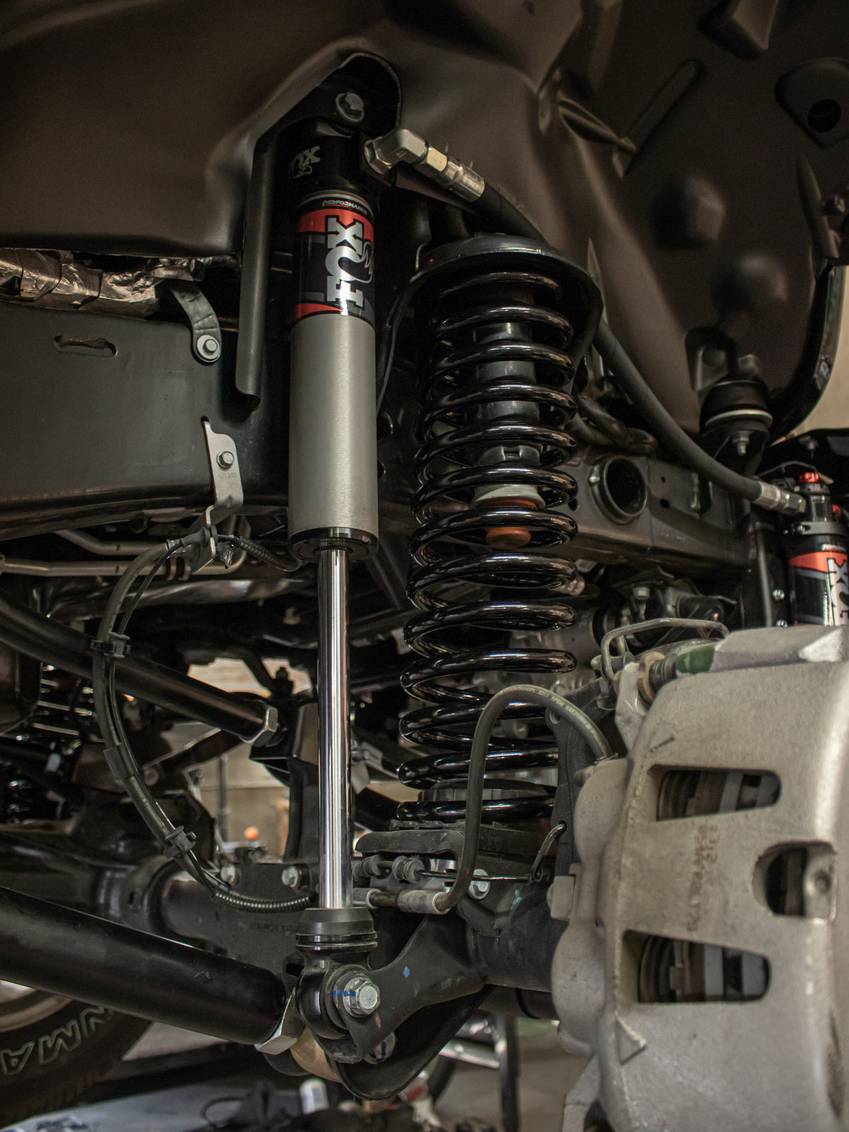 Close-up of a vehicle's suspension system featuring a silver and black KYB shock absorber, a black coil spring, and various metal suspension components.