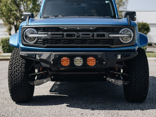 Front view of a blue Ford Bronco Raptor with a custom bumper and round amber lights