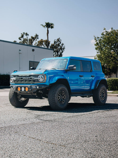 Front three-quarter view of a blue Ford Bronco Raptor with a bumper-mounted light bar on asphalt