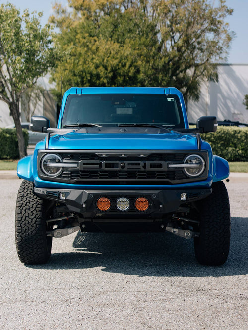 Head-on front view of a blue Ford Bronco Raptor with three round lights in its custom bumper
