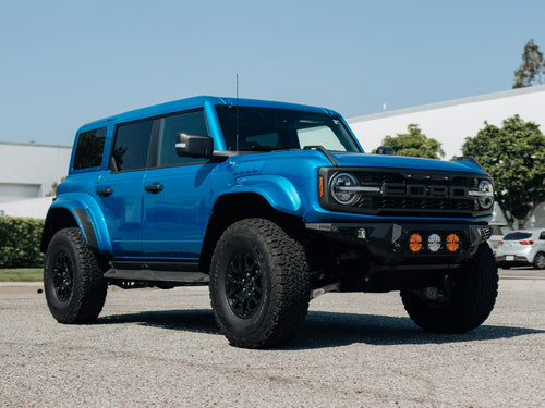 Low front three-quarter view of a blue Ford Bronco Raptor showing its wide fenders