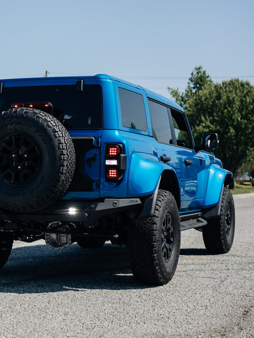 Rear three-quarter view of a blue Ford Bronco Raptor with the spare tire mounted on the tailgate