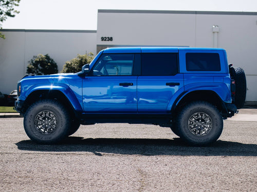 Side profile of a blue Ford Bronco Raptor with black wheels and a lifted stance