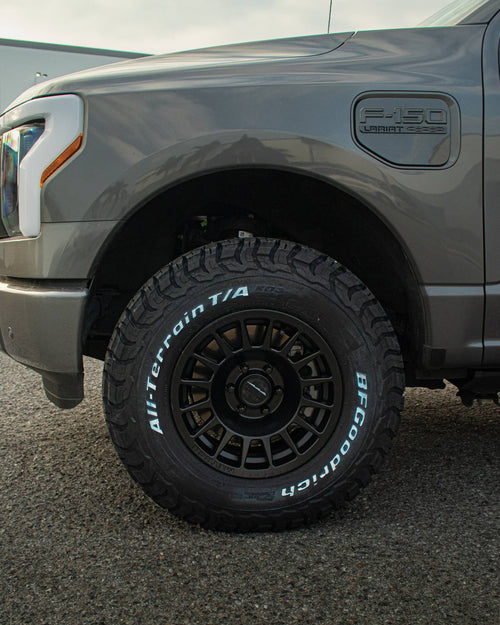 Black wheel with a BFGoodrich all-terrain tire on the front of a gray Ford F-150 Lightning
