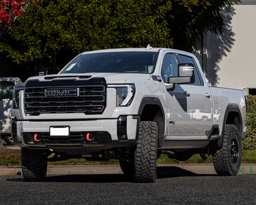 Front view of a silver GMC Sierra HD AT4 with a black grille and red tow hooks