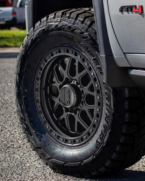 KMC wheel with a Toyo Open Country tire beneath the AT4 fender badge of a silver GMC Sierra HD