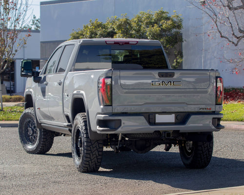 Rear three-quarter view of a silver GMC Sierra HD AT4 with black wheels