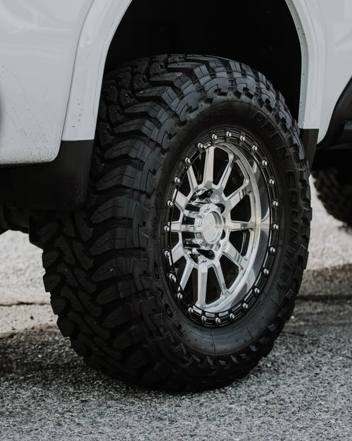 Close-up of a machined wheel with a Toyo mud-terrain tire in the fender of a white GMC Sierra 2500 HD