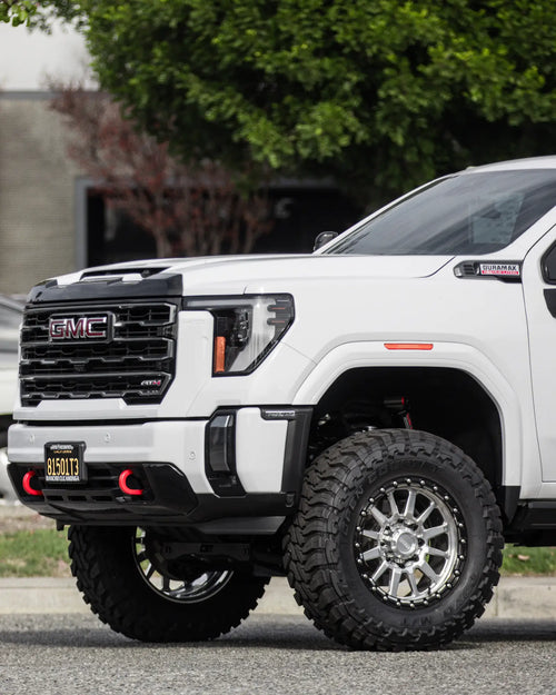 Front three-quarter view of a lifted white GMC Sierra 2500 HD AT4 showing the front tow hook