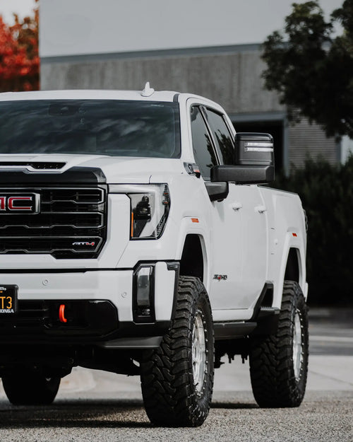 Front three-quarter close-up of a lifted white GMC Sierra 2500 HD AT4 with a red tow hook