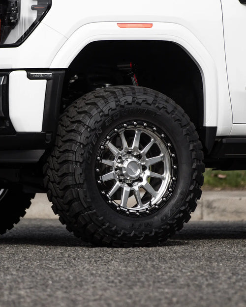 Close-up of the front wheel and fender of a white GMC Sierra 2500 HD AT4 with an amber marker light