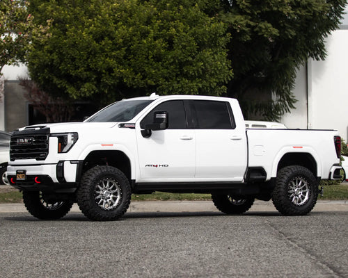 Side profile of a lifted white GMC Sierra 2500 HD AT4 in an industrial lot