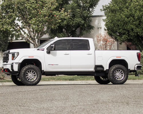 Side profile of a lifted white GMC Sierra 2500 HD AT4 on a tree-lined street