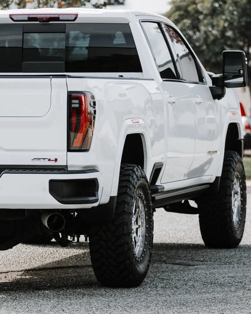 Rear corner of a lifted white GMC Sierra 2500 HD showing the tailgate, tail light and rear wheel