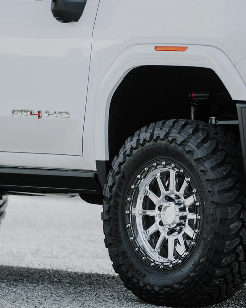 Close-up of an Innov8 wheel with a Toyo M/T tire and AT4 HD badge on a white GMC Sierra 2500 HD