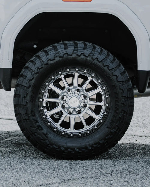 Close-up of a chrome-finish wheel with a mud-terrain tire in the wheel well of a white GMC Sierra 2500 HD