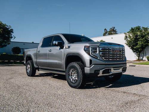 Front three-quarter view of a silver GMC Sierra Denali with a chrome grille and raised ride height
