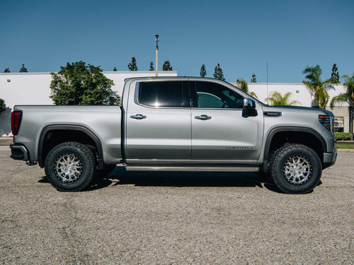 Full side view of a silver GMC Sierra Denali showing its lifted stance and chrome wheels