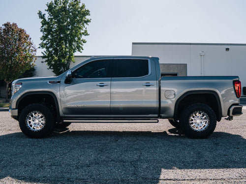 Side profile of a lifted silver GMC Sierra Denali crew cab parked on asphalt