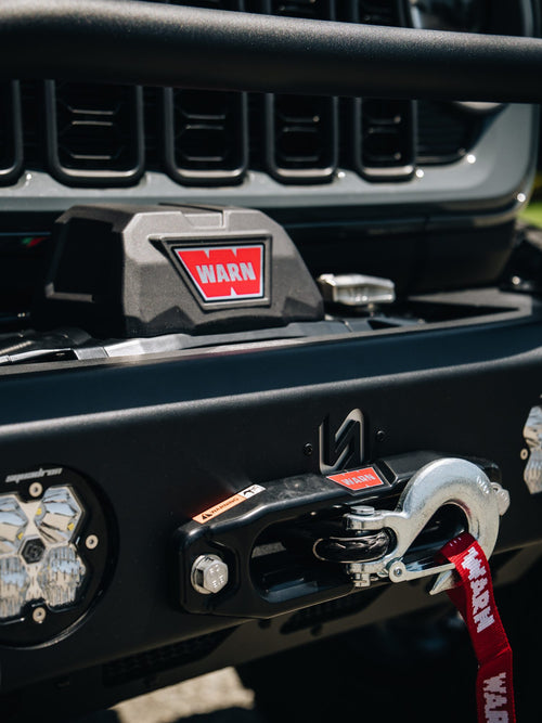 Close-up of a Warn winch and Baja Designs Squadron LED light on a Jeep Gladiator bumper