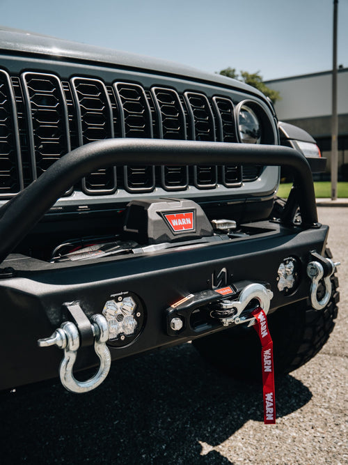 Close-up of a Warn winch bumper with shackles and a red recovery strap on a gray Jeep Gladiator