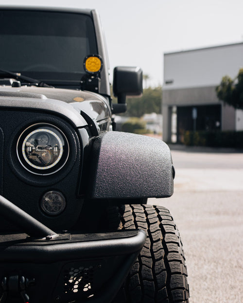 Close-up of the headlight, fender and all-terrain tire on a black Jeep Wrangler