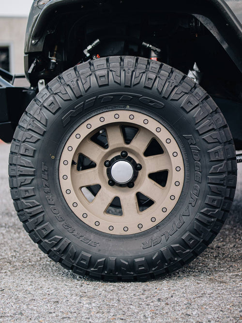 Bronze wheel and off-road tire on the front of a gray Jeep Wrangler Rubicon