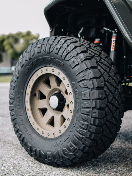 Nitto Ridge Grappler tire on a bronze beadlock-style wheel on a gray Jeep Wrangler Rubicon