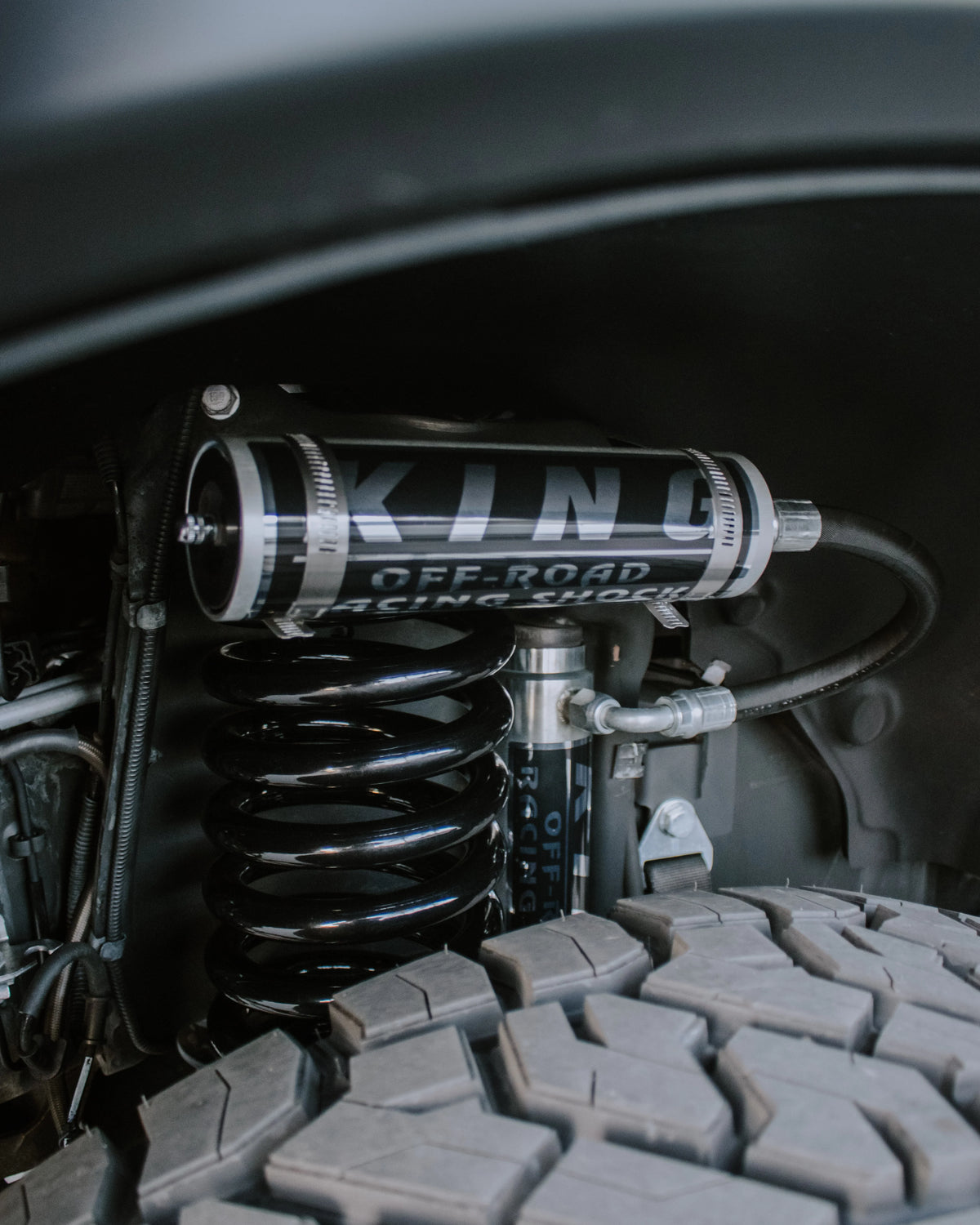 Close-up of a King remote-reservoir shock and heavy-duty coil spring installed behind an off-road tire.